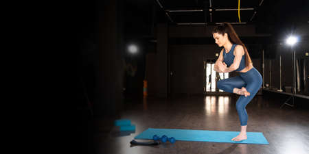 woman doing yoga in the gym, standing in yoga pose for balance, asana on one leg, healthy lifestyle and natural balance concept. banner.の写真素材