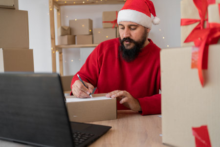 Happy bearded Santa Claus in suit with gift box on laptop while sitting at workshop table on Christmas Eve. online shopping sales on christmas holiday concept. e-commerceの写真素材