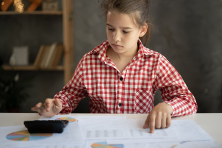 Little girl counting bills, calculating budget at home using calculator, working with financial documents at desk, paying bills online, managingの写真素材