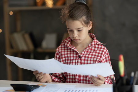 Focused young girl child looking through paper documents, managing business affairs, summarizing taxes, planning future investments, accounting alone at home office. Achievement careerの写真素材
