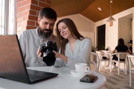 Colleagues photographers working in cafe using camera and laptop, viewing pictures on camera. New modern technologiesの写真素材