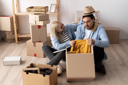 Young couple unpacking boxes with things and clothes moving to a new house, new apartment owners sitting on the floor with boxes, happy moving timeの写真素材