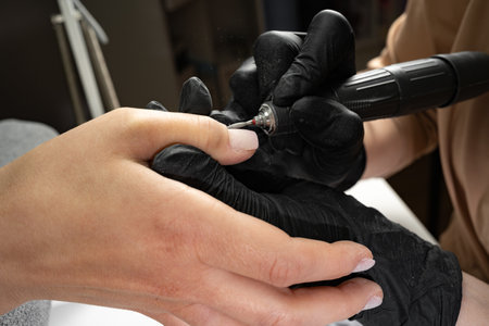 Woman uses electric nail file drill in beauty salon to trim and remove cuticles. Perfect manicure process.の写真素材