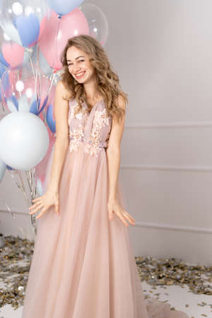 Beautiful laughing woman in dress holding balloons and looking at camera on pink background.の写真素材
