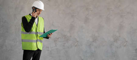 Builder manager. Male engineer speaks on phone. Construction paper plans from architect. Man in builders uniform isolated on background. Architect calls client. Construction company employee.の写真素材