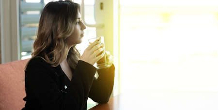 Brunette girl enjoying hot tea at cafe. Pretty woman drinks tea with lemon and relaxing at coffee shop. bannerの写真素材