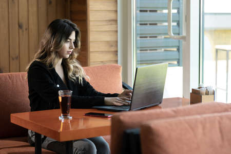 Serious young woman sitting in cafe working on laptop, charming freelancer girl thinking about new ideas while working with pc, technology or startup businessの写真素材