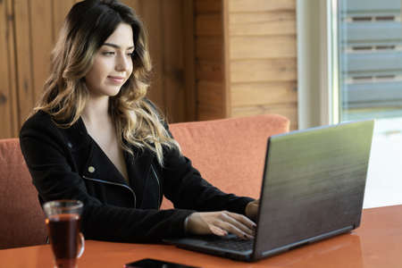 Portrait of young woman sitting in cafe working on laptop, charming freelancer girl thinking about new ideas while working with pc, technology or startup business conceptの写真素材