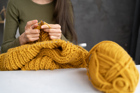 Close-up of female hands knitting wool sweater. Woman knits from thick yarn. Handmade clothes. The girl goes in for her hobbies. Knittingの写真素材
