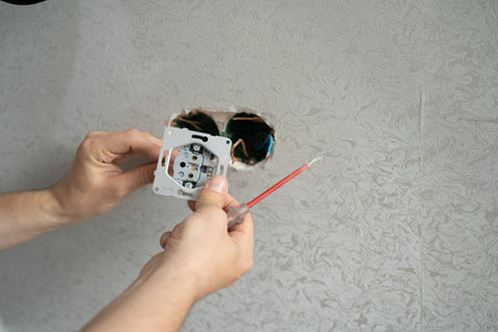 electrician connects the sockets to the electrical wires on the wall using a screw driverの写真素材