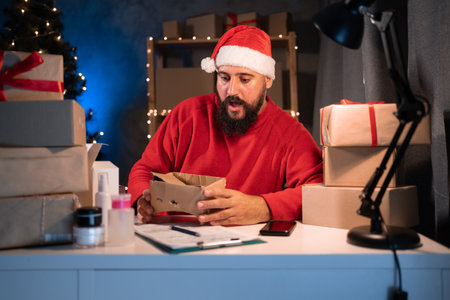 The concept of starting a small and medium business A young start-up entrepreneur, small business owner, wearing a santa claus hat, sits at a table and holds a broken box in his hands.の写真素材