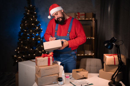 Small and Medium Business Startup Concept A young start-up entrepreneur, wearing a santa claus hat and work overalls, takes an order while standing and writes the delivery address on the box.の写真素材