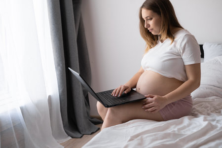 Pregnancy and technology. Pregnant woman using laptop at home, browsing Internet, shopping online or reading maternity blog, free spaceの写真素材