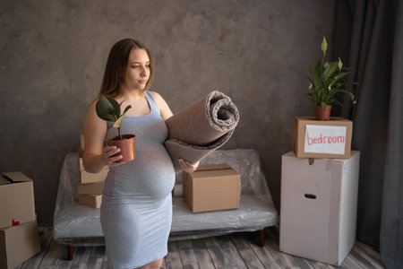 Pregnant woman alone in new apartment, standing in front of boxes during moving in new home, housing program for mothersの写真素材