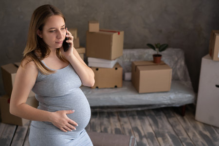 Young pregnant woman making a phone call to the transportation service, moving to a new apartment of a single motherの写真素材