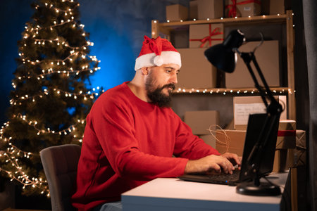 small business owner Indian freelance Santa working in home office using computer, online marketing packaging box and gifts for Christmas delivery, SME e-commerce Christmas saleの写真素材
