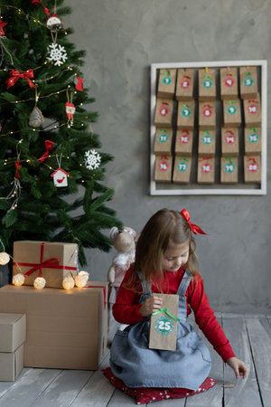 Christmas traditions concept, child with handmade Christmas advent calendar, girl holding package of sweets with number twenty five, handmadeの写真素材