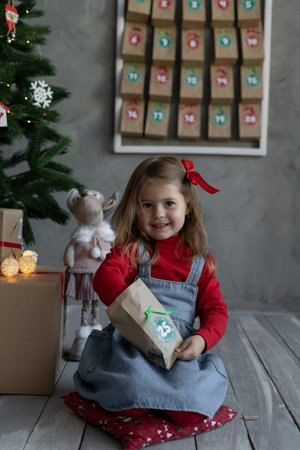 Advent calendar handmade for children. happy girl in casual clothes opening craft bag of candies with number, christmas kids fan, winter home traditionsの写真素材
