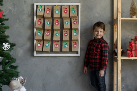 Child near handmade christmas advent calendar, craft candy packaging hanging on wall winter holiday eve, christmas kids fanの写真素材