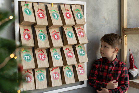 Handmade advent calendar hanging on the wall, child standing near craft bags with sweets, Christmas baby joysの写真素材
