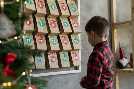 Handmade advent calendar hanging on the wall, child standing near craft bags with sweets, Christmas childrens joyの写真素材