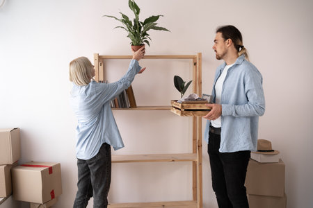 Apartment owners man and women move to a new house, unpack things put flowers on the shelf, moving and renovationの写真素材