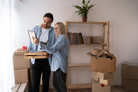happy couple looking at photo and unpacking things at new home. people, family, memories and movingの写真素材