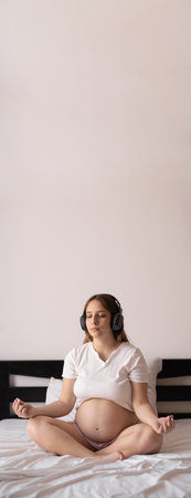 Motherhood meditation. pregnant woman meditating while sitting in lotus position on bed. vertical banner, emptyの写真素材