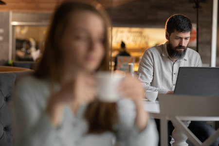 successful business man sitting at the cafe working on a laptop, girl is blurred on foreground, work of freelancerの写真素材