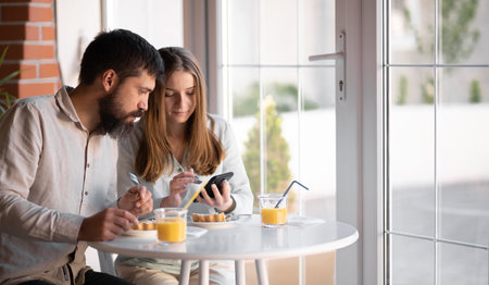 Portrait of beautiful young couple having a break time in cafe, he is showing her something funny in his mobile phone, enjoyingの写真素材