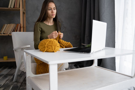 Seriously woman with knitting yarn and needles learn how to knit using website on a laptop at home.following a tutorial channel on computer to learn knitting work wool activity for her hobbiesの写真素材