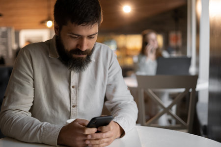 Male student using smartphone while sitting in cafe, lunch break in coffee shop, businessman working in restaurantの写真素材