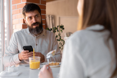 Happy young couple having breakfast in cafe, enjoying together using cell phone. Cafe or restaurant interior.の写真素材