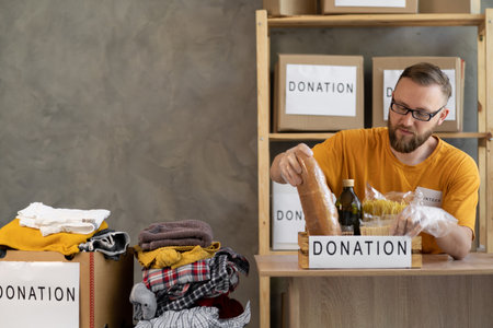 Portrait of smiling man volunteer packing a donation box in office. charity, donation and volunteering conceptの写真素材