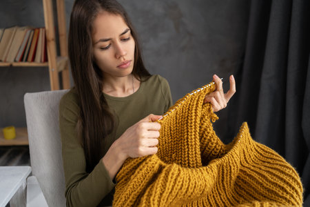 Beautiful girl knits a warm sweater on armchair. Knitting as a hobby. Accessories for knitting.の写真素材