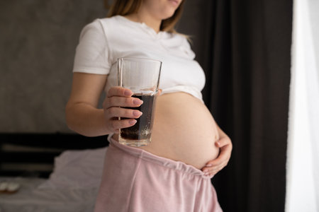 Close up of a pregnant belly and junk food.Cola and pregnancy. Pregnant female unhealthy motherhoodの写真素材