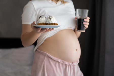 Close up of a cute pregnant belly tummy and junk food. Cake and pregnancy. Pregnant female unhealthy and healthy motherhoodの写真素材