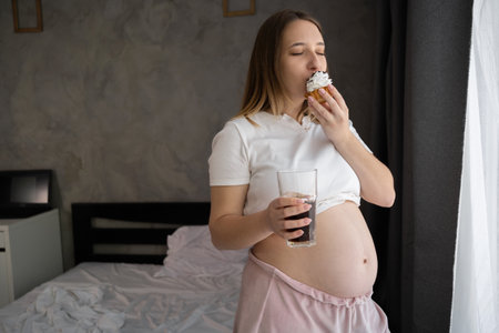 Pregnant woman eats cakes and drinks cola water. Pregnancy and unhealthy eatingの写真素材