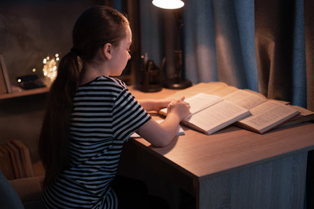 Young girl studying at desk in bedroom in evening, homeschoolingの写真素材