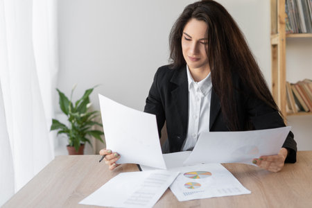Serious latin business woman working in office with documents. Women working arrange documents with papers on the office deskの写真素材