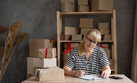 Shipping shopping online, elderly woman start up small business owner writing address at workplace.small business entrepreneur SME or freelance woman working with boxの写真素材