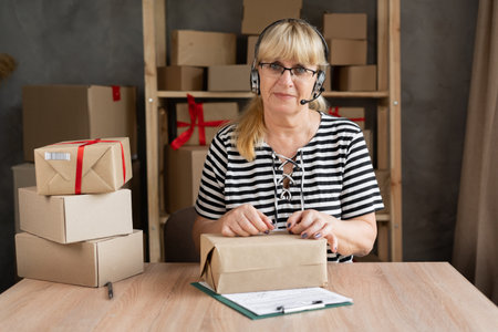 Smiling female small business owner sit at desk in home office talk on webcam with client wearing headset, middle-aged woman in headphones have video call consult customer online, smeの写真素材