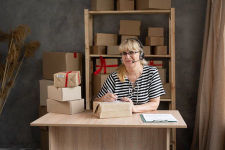 start up Small business owner elderly woman in headphones taking and placing order while working at home office, SME telemarketing e-commerceの写真素材