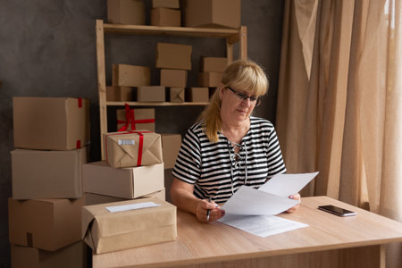 Small business entrepreneur SME working with box at home, elderly woman reading document at table on warehouse, SME e-commerce technologyの写真素材