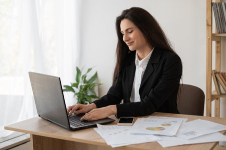 Portrait of a beautiful woman data analyst sitting at a desk working on a laptop. Stylish woman in an office setting. Searching for solutionの写真素材