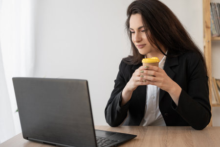 Adult happy hispanic businesswoman talking online chat meeting holding coffee using laptop in virtual office. College female student learning remotely.の写真素材