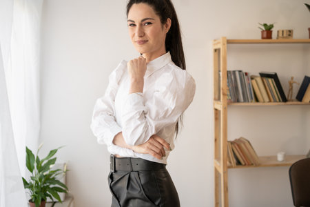 Happy businesswoman smiling and posing with arms crossed in front of office windowの写真素材