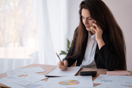 Latin businesswoman talking on the phone and taking notes working in office. Businessの写真素材