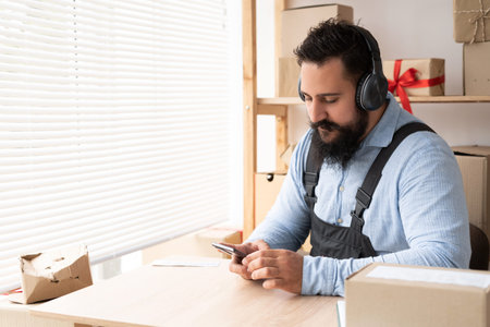 Indian businessman listening to music by headphones and smartphone while working in working space....