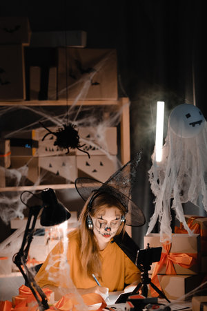 Startup small business entrepreneur or freelance caucasian woman in halloween makeup taking order online video call using smart phone. online marketing packaging box and shipping. copy space.の写真素材